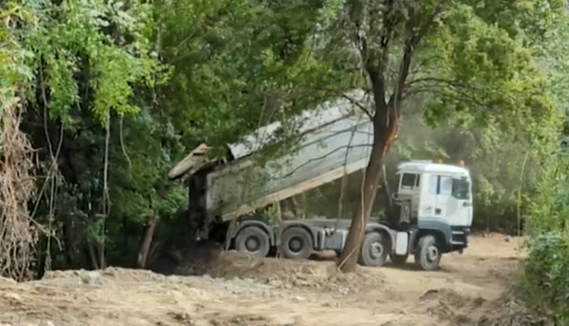 Видео показва как тежки камиони изхвърлят строителни отпадъци в дере.