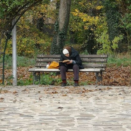 Възрастна жена на пейка и с книга в ръка