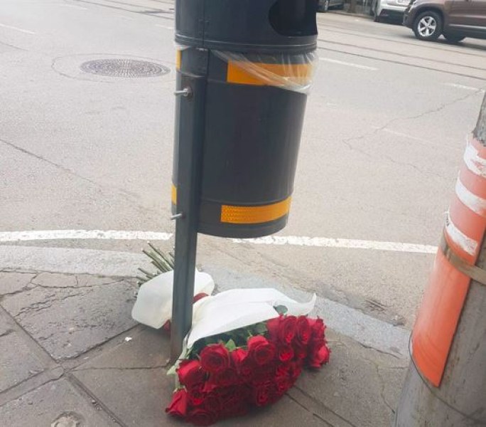 Снимка на красив букет рози, захвърлен до кофа за боклук