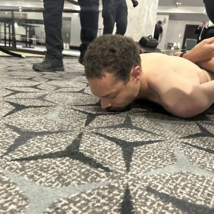 Мъж без риза лежи на пода а до него стоят